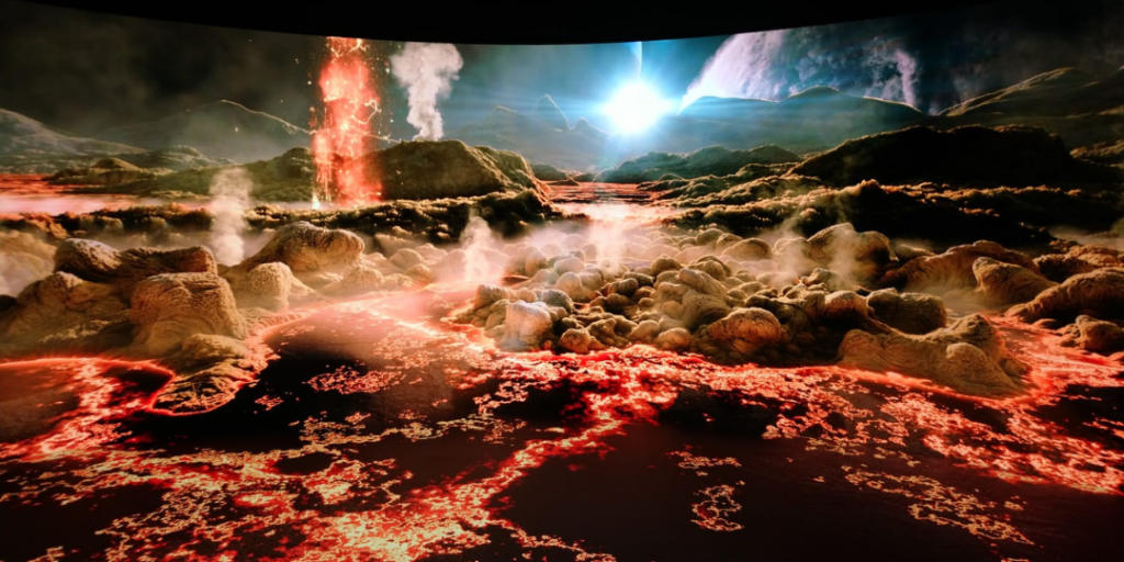 Immersive AV Design: National Space Centre | Audiotek Volcanic landscape with glowing lava, steam rising from rocky ground, and distant mountains under a bright sky.