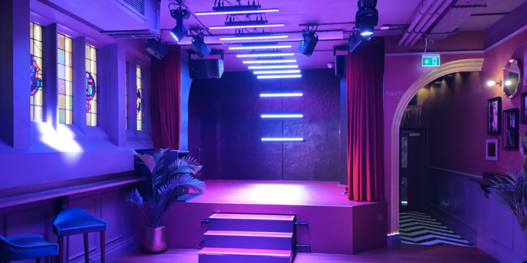 Intimate on-stage area with purple neon lights, red curtains, and three-step platform in a lounge venue.